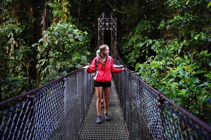 Hikers crossing a hanging bridge before a hot springs soak on a La Fortuna waterfall Arenal volcano hot springs tour, Costa Rica
